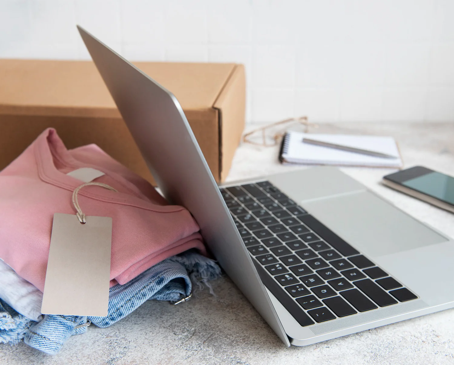 Laptop en una mesa con una caja, ropa y celular.